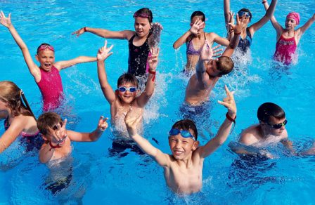 fotografia przedstawia grupę uśmiechniętych dzieci, znajdujących się w basenie